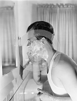 Profile of a young man in front of a mirror in a bathroom shaving