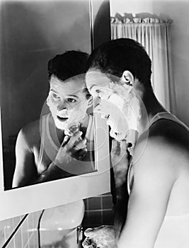 Profile of a young man in front of a mirror in a bathroom shaving