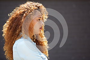 Profile young woman with curly hair against gray wall
