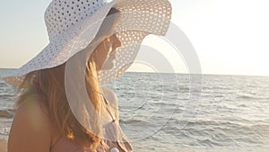 Profile of a young woman in a hat with wide brim from the sun against the background of the sea, a girl enjoying nature at sunrise