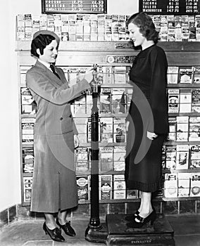 Profile of a young woman in an uniform measuring weight of another young woman on a weighing scale