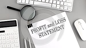 PROFIT AND LOSS STATEMENT written on paper with office tools and keyboard on the grey background