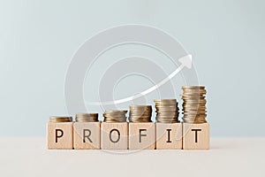 PROFIT text on wooden cube blocks with stack of coin above and increasing graph. For financial investment concept