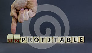 Profitable or unprofitable symbol. Businessman hand turns cubes and changes word `unprofitable` to `profitable`. Beautiful gre