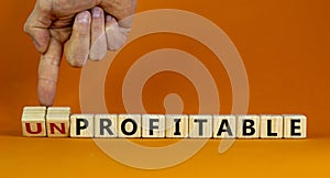Profitable or unprofitable symbol. Businessman hand turns cubes and changes word `unprofitable` to `profitable`. Beautiful ora