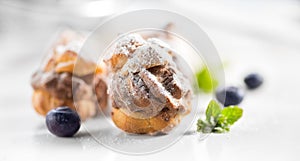 Profiterole or cream puff with filling, powdered sugar topping with berries, on white background