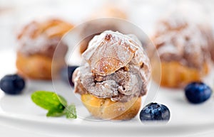 Profiterole or cream puff with filling, powdered sugar topping with berries, on white background