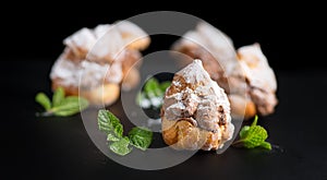 Profiteroles or cream puff with filling, powdered sugar topping, on black background.