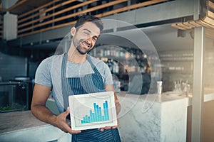 Profiting from his passion. Portrait of a young man holding a digital tablet with a graph on the screen at a coffee shop