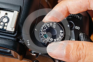 Program dial mode on dslr camera with fingers on the dial