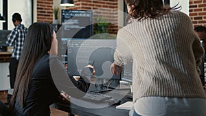 Programer pointing pencil at computer screen with software compiling code explaining source algorithm to coworker