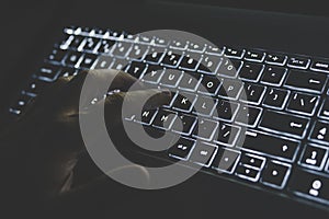 Programmer or computer hacker typing code on laptop keyboard. keypad is lit in white light. hand presses a key on your computer