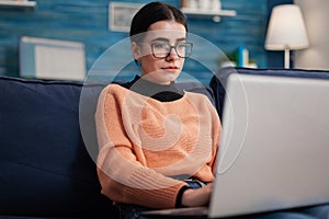 Programmer with glasses holding laptop on sofa writting code.