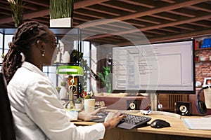 Programmer in home office looking at UI on PC screen, typing code