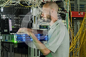 A programmer with a laptop is in the room with computer equipment. The system administrator works in the server room of the data