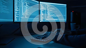 Programmer Typing Code on Backlit Keyboard with Multiple Screens in Dark Room