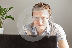 Programmer working from home, remote, home office. A man with glasses looks at the monitor. Remote work concept