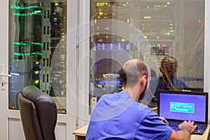 The programmer works in a modern data center. System administrator with a laptop sits in front of the glass door of the server