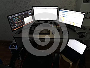 Programmer workspace with multiple monitors and laptop in dark room