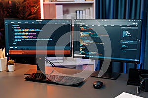 Programming code on computer two screen on desktop at neon light room. Infobahn.