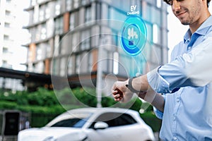 Progressive businessman check wearable hologram watch on EV car battery's status