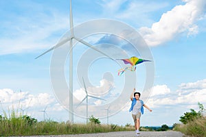 Progressive happy boy running and flying kite with wind turbine background