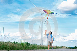 Progressive happy boy running and flying kite with wind turbine background