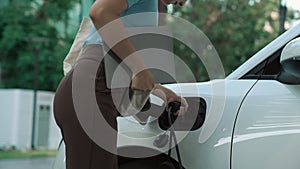 Progressive woman installing plug from home charging station to electric vehicle