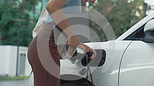 Progressive woman installing plug from home charging station to electric vehicle