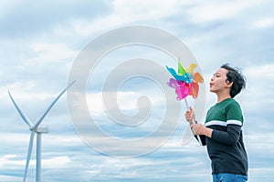 Progressive young asian boy playing with wind pinwheel toy at wind turbine farm.