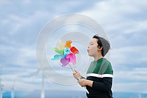 Progressive young asian boy playing with wind pinwheel toy at wind turbine farm.