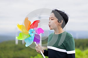 Progressive young asian boy playing with wind pinwheel toy at wind turbine farm.