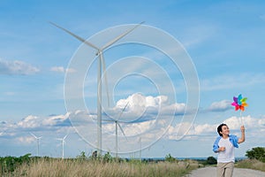 Progressive young asian boy playing with wind pinwheel toy at wind turbine farm.