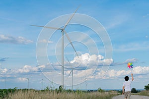 Progressive young asian boy playing with wind pinwheel toy at wind turbine farm.