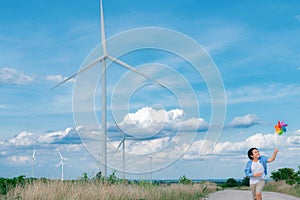 Progressive young asian boy playing with wind pinwheel toy at wind turbine farm.