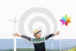 Progressive young asian boy playing with wind pinwheel toy at wind turbine farm.