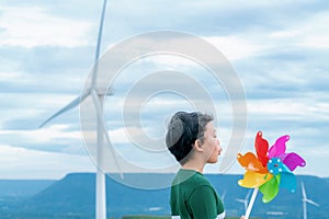 Progressive young asian boy playing with wind pinwheel toy at wind turbine farm.