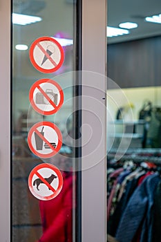 Prohibition signs near the entrance to the clothing store. Stickers on the glass window near the door with prohibitions.