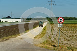 A prohibitory sign indicating that cars and motorcycles are prohibited from driving on a dirt road in a field.