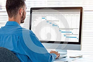 Project manager in office scheduling tasks and progression of milestones completion with Gantt chart planning on computer,