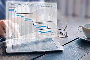 Project manager updating progress and deliverables milestones schedule on gantt chart planning with digital tablet computer,