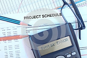 Project schedule With gant chart, eyeglasses, pencil, pen and calculator showing syntax error message.