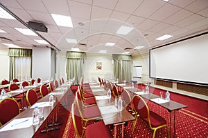 Projector, white screen, red chairs and tables