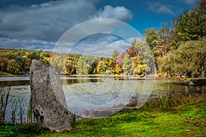 Prominent boulder displayed under dramatic crisp autumn sky over Tyrrel Lake at Innisfree Garden, Millbrook, New York