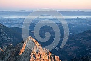 Prominent peak catching sunrise light with mountain range and foggy valley in the background