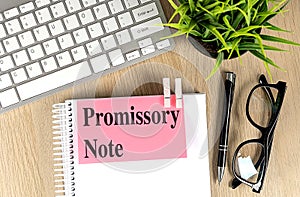 PROMISSORY NOTE text pink sticky on notebook with keyboard, pen and glasses photo