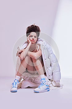 Promotion for winter clothing lines. Young beautiful woman in sneakers, sleepwear sitting on floor, wearing warm coat on