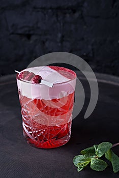 Promotional shot of a red alcoholic cocktail for parties. With a green sprig of mint and decorative raspberries. On a dark