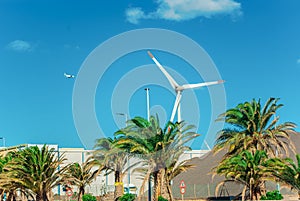 Propeller of a wind power plant near a parking lot with palm trees and trees