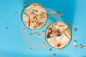 Proper nutrition, breakfast. Welness - granola with yogurt and fruits: banana and apple, in glass cups on a blue background, top